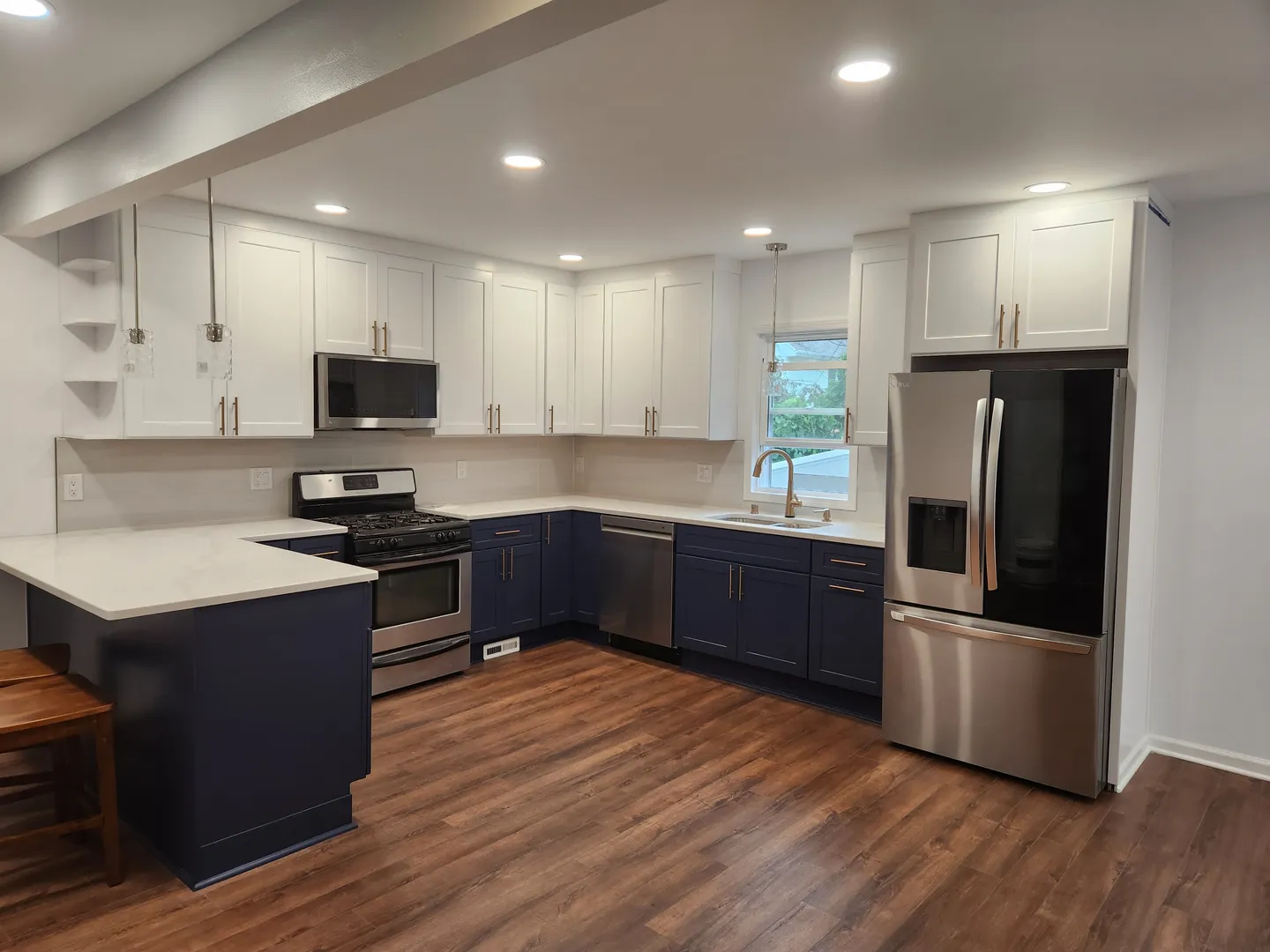 Modern kitchen with hardwood floors, navy lower cabinets, white upper cabinets, stainless steel appliances, and a central island with wooden stools.