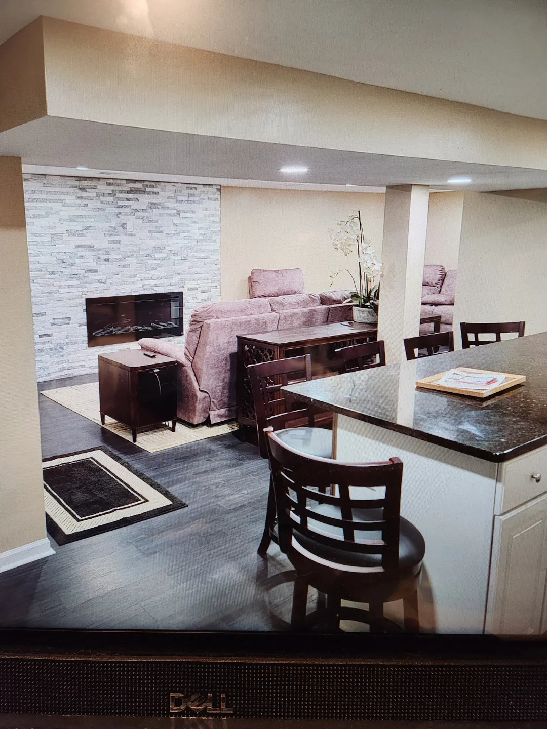 Basement living area with a fireplace, brown sectional sofa, and bar stools at a granite countertop. White cabinets and a small stack of books are visible.