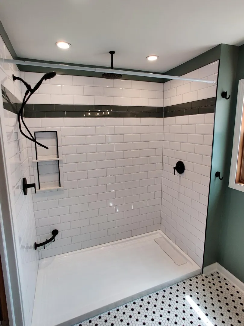Modern shower with white subway tiles, a dark horizontal accent strip, matte black fixtures, niche for storage, and patterned floor tiles, lit by recessed ceiling lights.